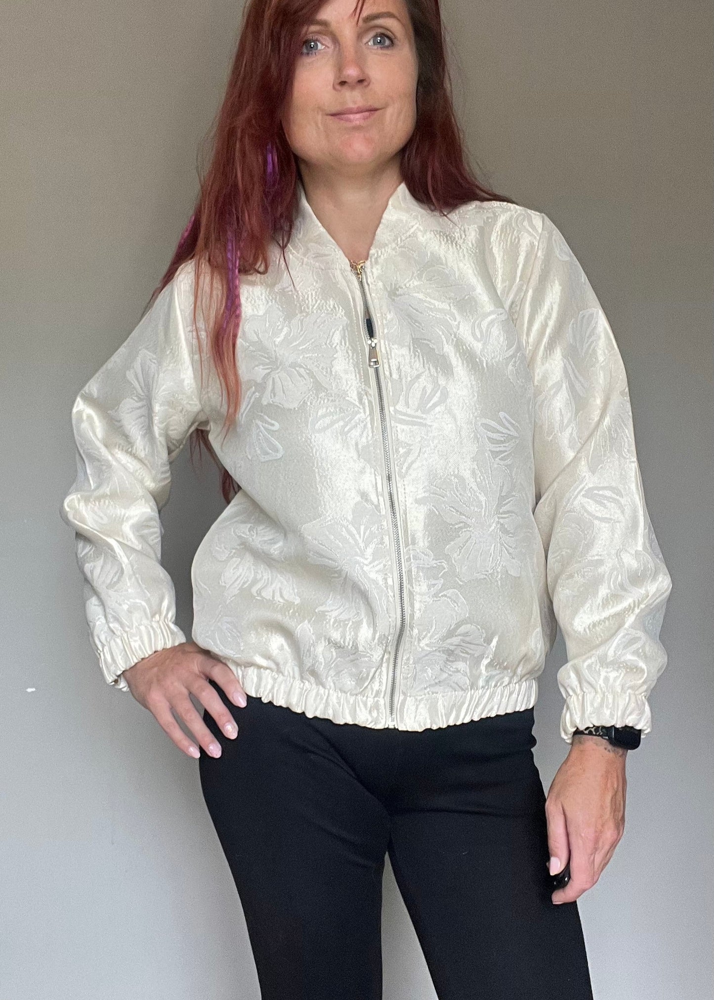 Champagnekleurig semi bomberjasje van glanzende stof met bloemenprint, rits en steekzakken. Vrouwelijk, trendy en one size.