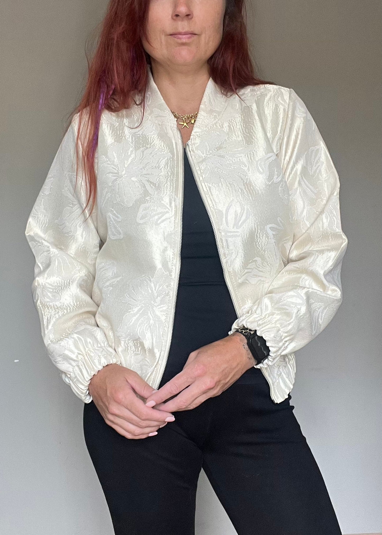 Champagnekleurig semi bomberjasje van glanzende stof met bloemenprint, rits en steekzakken. Vrouwelijk, trendy en one size.
