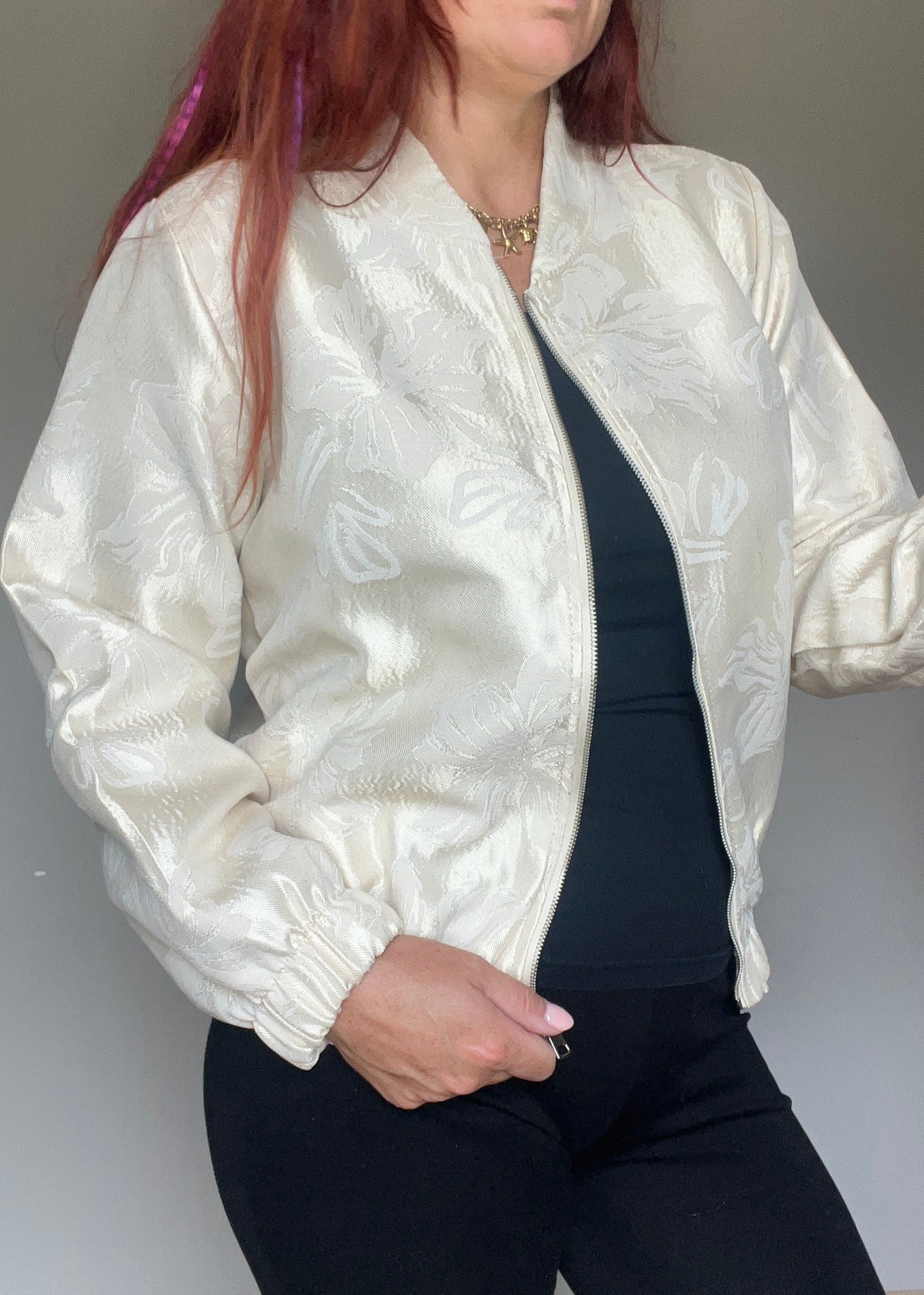 Champagnekleurig semi bomberjasje van glanzende stof met bloemenprint, rits en steekzakken. Vrouwelijk, trendy en one size.