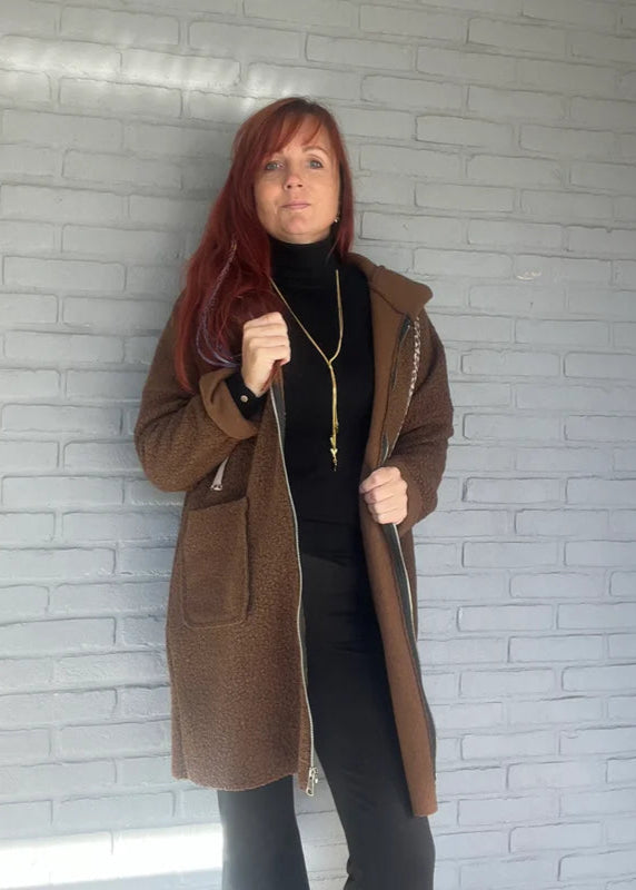 Bruin langer model jasje van wollige stof met rits, capuchon en zakken. Oversized fit, one size tot maat 44.