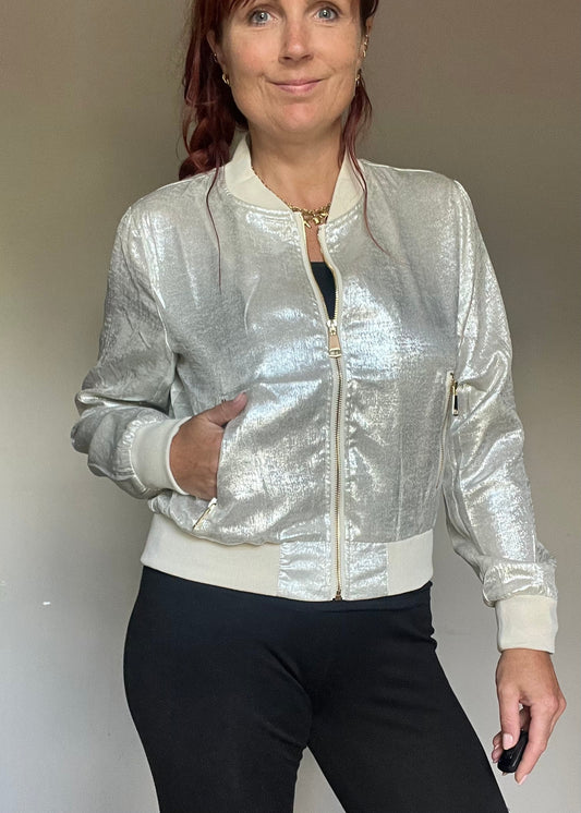 Metallic bomberjasje in goud of zilver met rits en steekzakken. Trendy, vrouwelijk model voor zomer en najaar.
