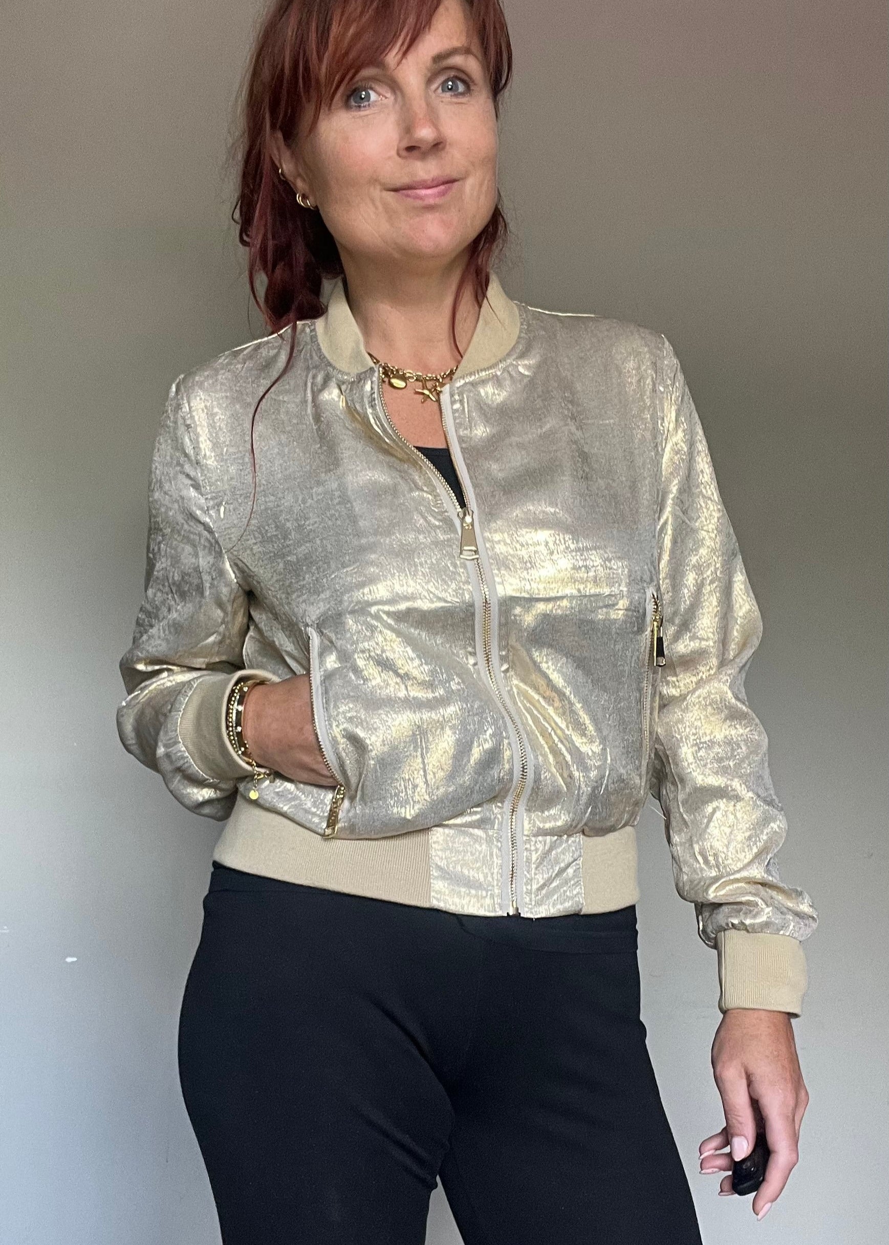 Metallic bomberjasje in goud of zilver met rits en steekzakken. Trendy, vrouwelijk model voor zomer en najaar.